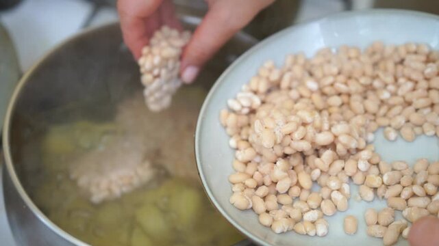 A person is cooking beans in a pot and transferring them to a white plate. The beans are in the process of being cooked and are being transferred to a plate.