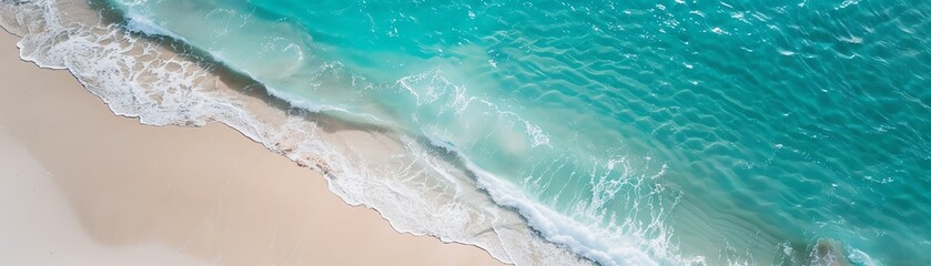 Aerial view of turquoise ocean waves gently crashing on the sandy beach, showcasing serene coastal beauty.