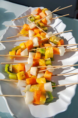 Buffet with varied fruits skewers in a tray. Detail of a ceramic tray with cubes of assorted pieces of fruits.