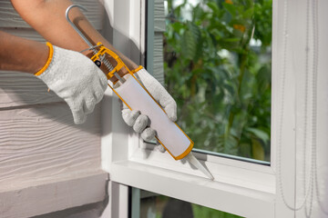 Construction worker using silicone sealant caulk for repair leaked inside window frame.