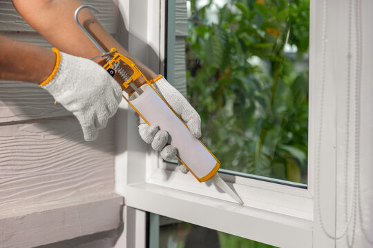 Construction worker using silicone sealant caulk for repair leaked inside window frame.