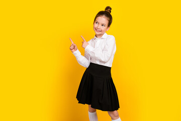 Photo of cute schoolgirl point fingers empty space wear uniform isolated on yellow color background