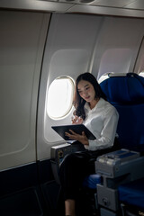 A woman is sitting on an airplane and looking at a tablet