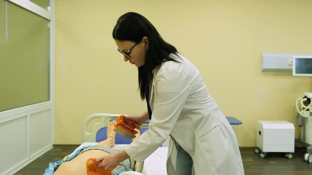 A female doctor at a medical school shows the operation of a defibrillator on a model mannequin. Dummy model for teaching medical practice. Close-up