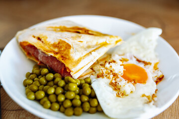 breakfast scrambled eggs hot sandwich with ham and cheese, green peas, legumes on plate