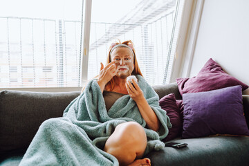 portrait middle-aged woman with cosmetic mask on face on sofa at home