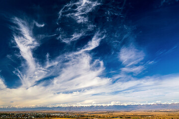 Panoramic view of Karakol City and scenic Kungey Alatau (Kungoy Ala-Too) Mountain Range, northern Tien Shan. Issyk-Kul Lake Region, Kyrgyzstan. Popular Asian tourist destination. Dry yellow grass.