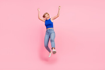 Full size photo of pretty young woman jump raise fists empty space wear blue top isolated on pink color background