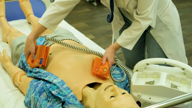 A female doctor at a medical school shows the operation of a defibrillator on a model mannequin. Dummy model for teaching medical practice. Close-up