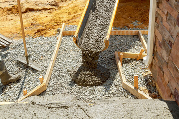 Construction worker pours cement on side of house to create new sidewalk that will stretch along...