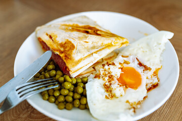 breakfast scrambled eggs hot sandwich with ham and cheese, green peas, legumes on plate