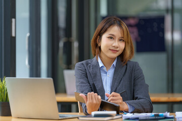 Young Asian women hand-holding and using digital tablets, work on laptop computers with books on the desk at home.