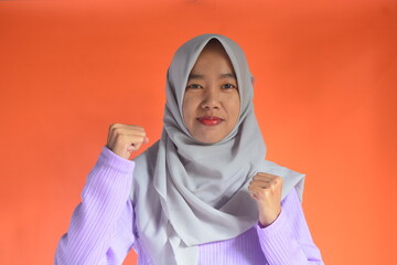Portrait of an Asian Muslim woman with an enthusiastic and powerful boxing stance, isolated on an orange background