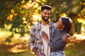 Loving Young Couple Hugging Against Background Of Autumn Leaves In Garden Or Countryside