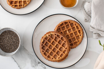 Homemade oatmeal and chia seed waffles on a white plate, accompanied by honey and ingredients