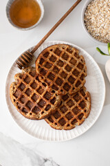 Homemade oatmeal and chia seed waffles on a white plate, accompanied by honey and ingredients
