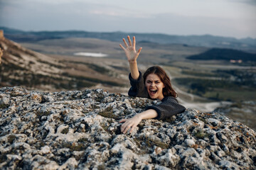 triumphant woman standing on mountain summit with arms raised in victory and smiling brightly