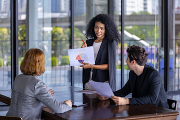 Young African woman sale manager is showing annual report chart to her colleagues in the executive meeting for next year plan with market share pie chart for global business and investment concept
