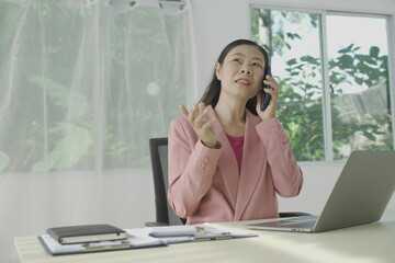 Happy young businesswoman in bright colored shirt uses computer and laptop in modern office Smiling manager while working on finance and marketing project Drink tea or coffee from a glass