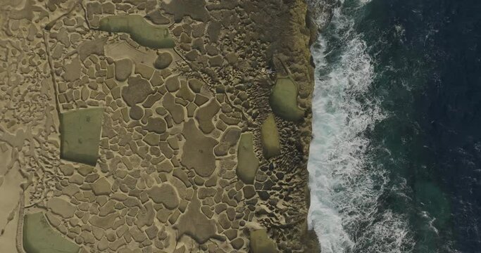 Aerial view of salt pans and coastline with rocky shoreline and blue water, Zebbug Gozo, Malta.