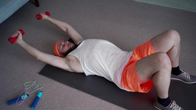 muscular Caucasian man doing dumbbell chest presses with hands while lying on a training mat on the floor. fitness at home
