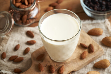 A glass of vegan almond milk on a wooden table, with almonds and raisins