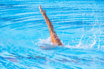 Female swimmer legs point up out of the water in swimming pool
