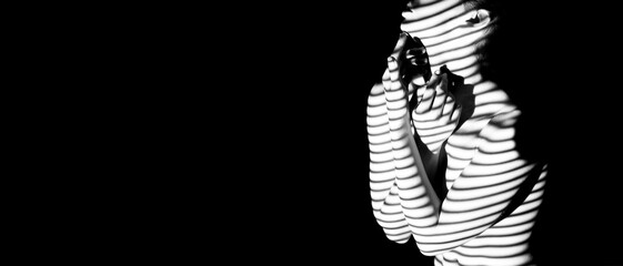 A black and white image of a woman standing in a darkened room. Her body is illuminated by a light...
