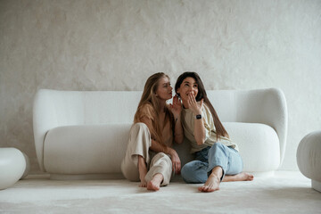 Telling a secret. Two happy young female best friends are indoors