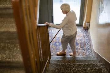 Elderly woman walking down the stairs leaning on a wooden cane
