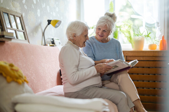 Senior woman and her adult daughter looking at photo album together 

