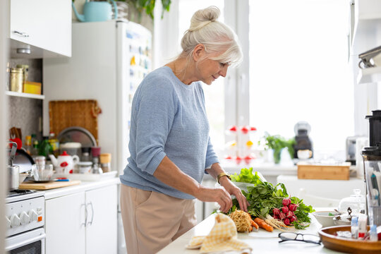 Senior woman preparing vegetable salad in kitchen at home
