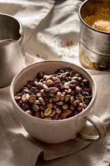 Detail of a cup filled with coffee beans on a beige tablecloth.