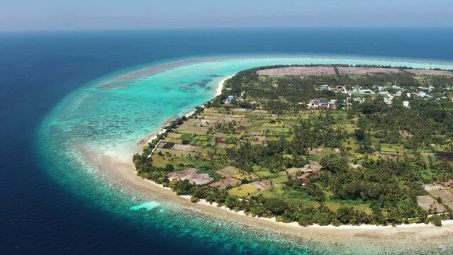 Aerial view of fields, lagoon, reef, corals, houses, and coastline in Thoddoo Atoll, Maldives.