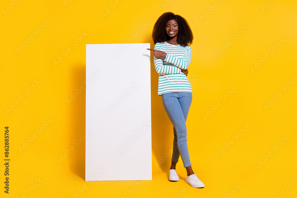 Poster Full length photo of attractive satisfied girl indicate finger empty space large phone isolated on yellow color background