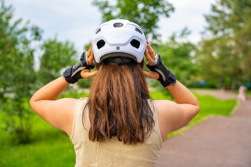 Portrait of roller skater woman putting on helmet in inline skates before rollerblading in park. Outdoor activities. Summer roller skating. © dtatiana