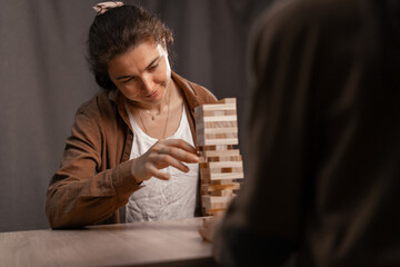 Female friends sitting and playing tower wooden block game together at home interior.