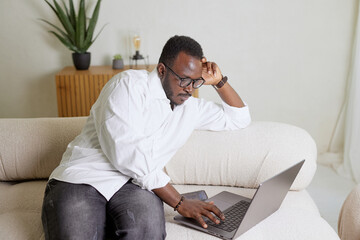 Handsome black African American man working on a laptop computer while sitting on a sofa