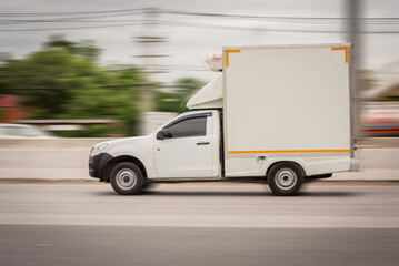 Motion blurred image, of a small white truck for logistics on the roads.