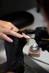 A close-up shot of a nail technician wearing black gloves, meticulously applying nail art to a...
