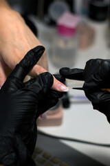 Close-up of a nail technician wearing black gloves, meticulously applying gel polish to a client's...