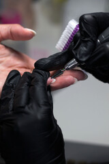 Fototapeta premium A manicurist in black gloves uses an electric nail file on a client's nails, focusing on precision and cleanliness in a professional nail care setting.