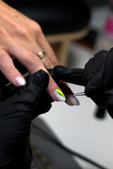  A professional manicurist in black gloves applying intricate green nail art to a client's nails, highlighting precision and creative design in a salon setting.