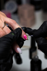  A manicurist in black gloves carefully applying pink and green nail art to a client's nails, highlighting detailed design and precision in a professional salon.