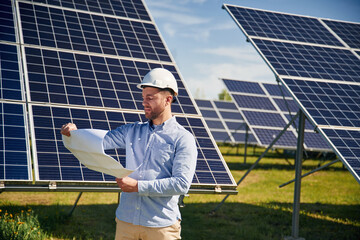 Reading the plan on paper. Engineer with photovoltaic solar panels outdoors at daytime