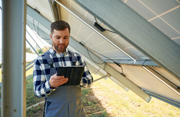 Under the photovoltaic solar panel and with digital tablet. Engineer outdoors at daytime