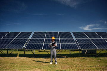 Black notepad in hands. Engineer with photovoltaic solar panels outdoors at daytime