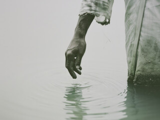 Hands of a man in white robe in the water.