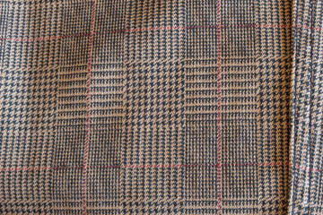 Close up of a classic checkered tweed blazer fabric, featuring a pattern of beige and dark tones...