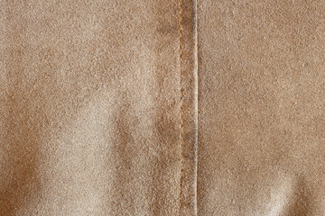Fototapeta premium Close-up of a beige textured fabric with vertical seam, showcasing its fine, soft surface and precise seams, highlights the fabric’s luxurious texture and the natural color of the leather.